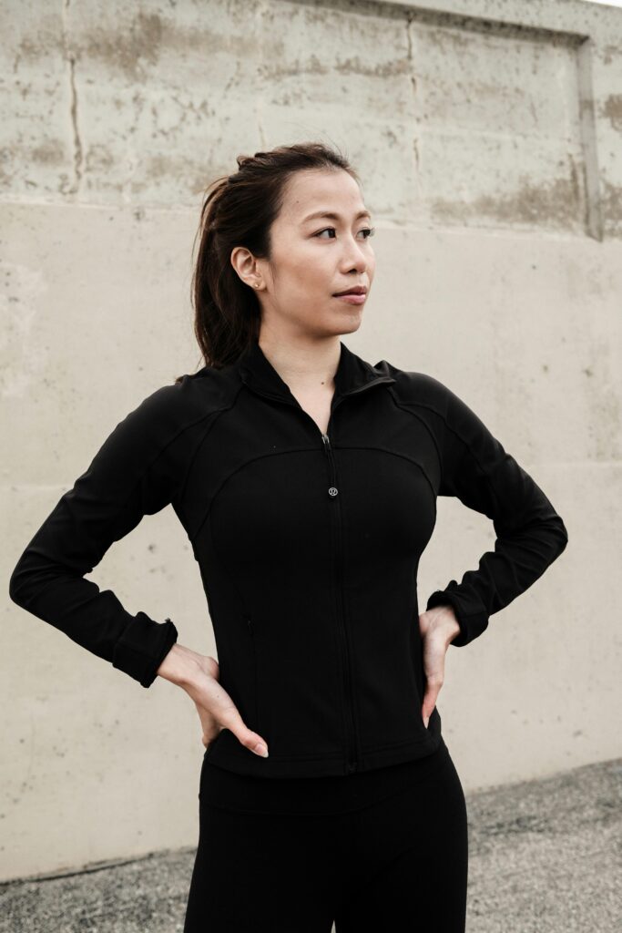 Woman in black athletic wear standing confidently outdoors, embodying empowerment and fitness.
