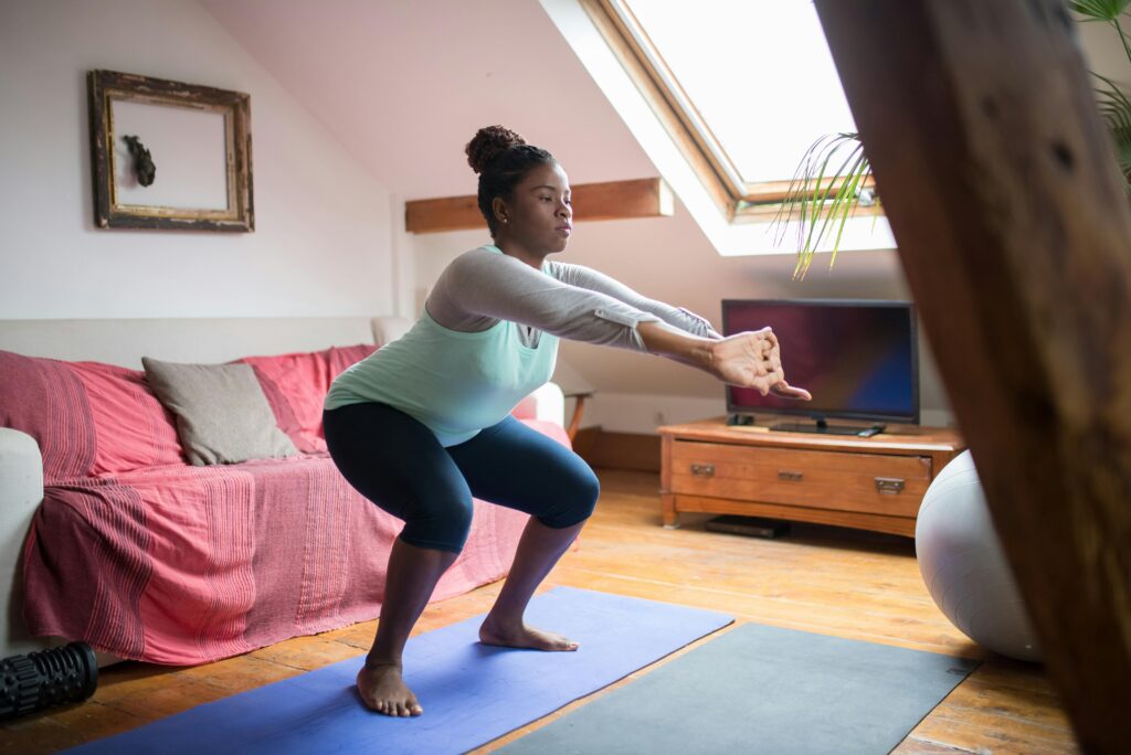 A woman performs squats on a yoga mat in a cozy living room, promoting home fitness and wellness.
