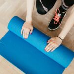 female in leggings and sneakers unfolding sport mat for practicing pilates in morning at home