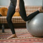 Woman performing home exercise routine using an exercise ball, wearing black leggings.