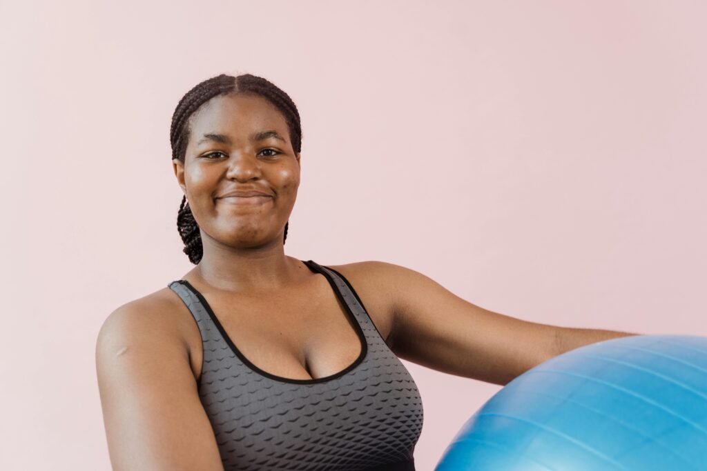 Smiling woman in sports attire holding an exercise ball, embodying wellness and a healthy lifestyle.